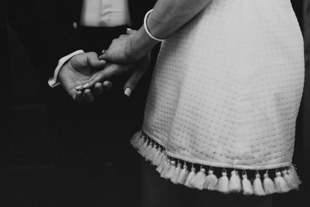 Bride in pearl bracelet and short fringe dress holding grooms hand