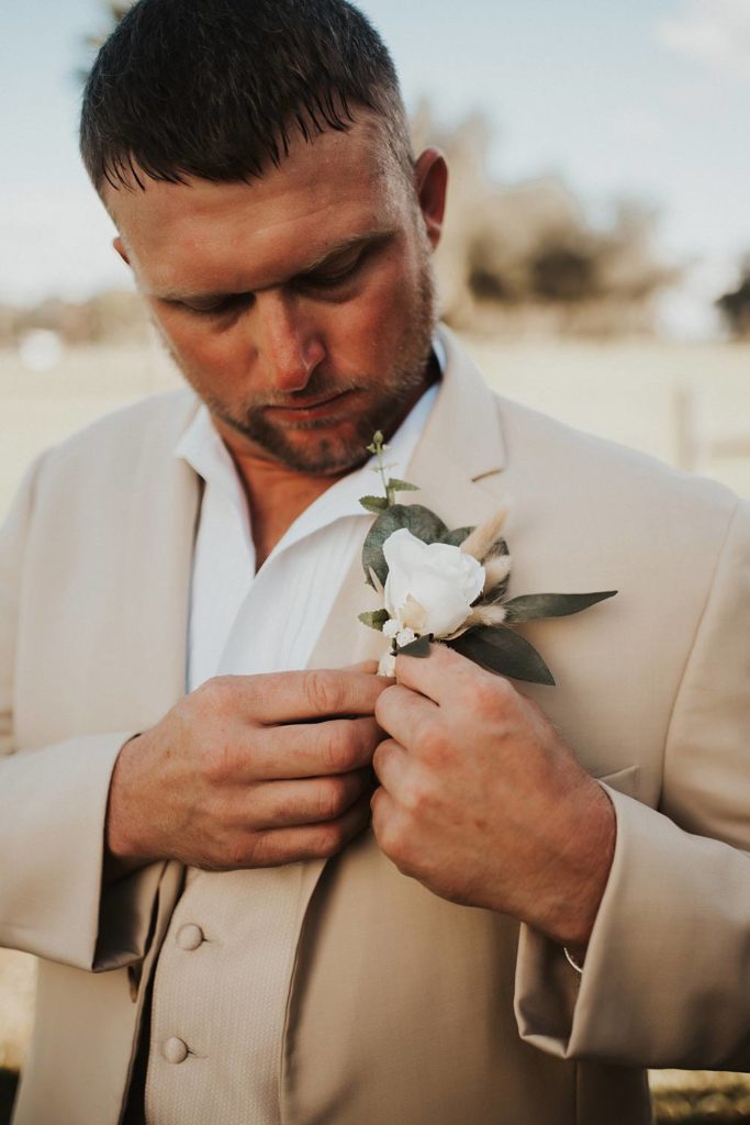 Groom pinning floral boutonniere while getting ready prior to Okeechobee, Florida wedding