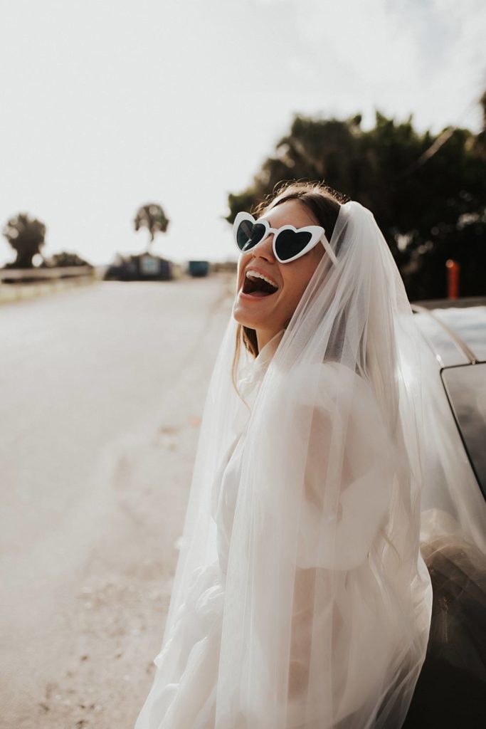 Bride in sunglasses with veil leaning on car