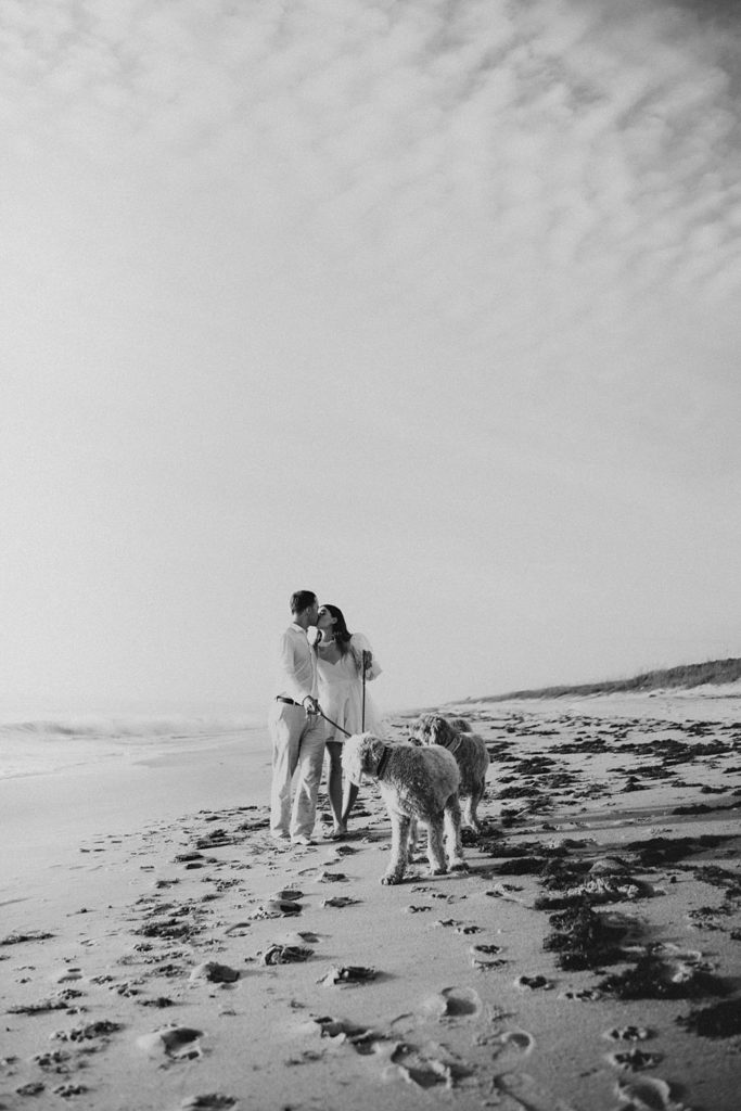 Bride and groom walking golden doodle dogs on beach