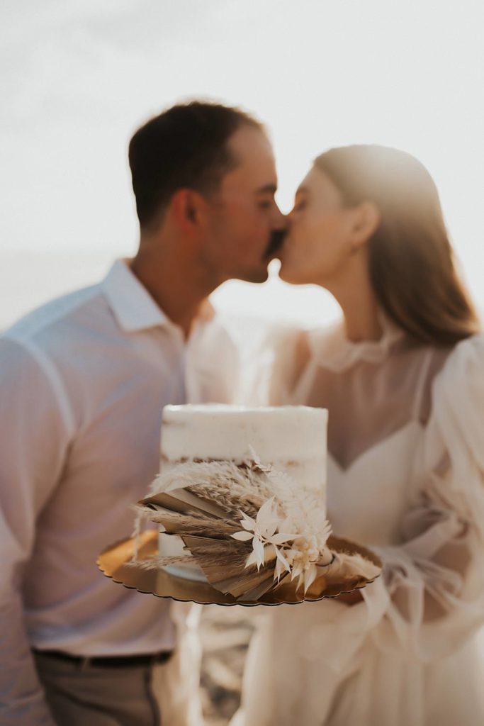 Bride and groom kissing behind rustic mini layered cake