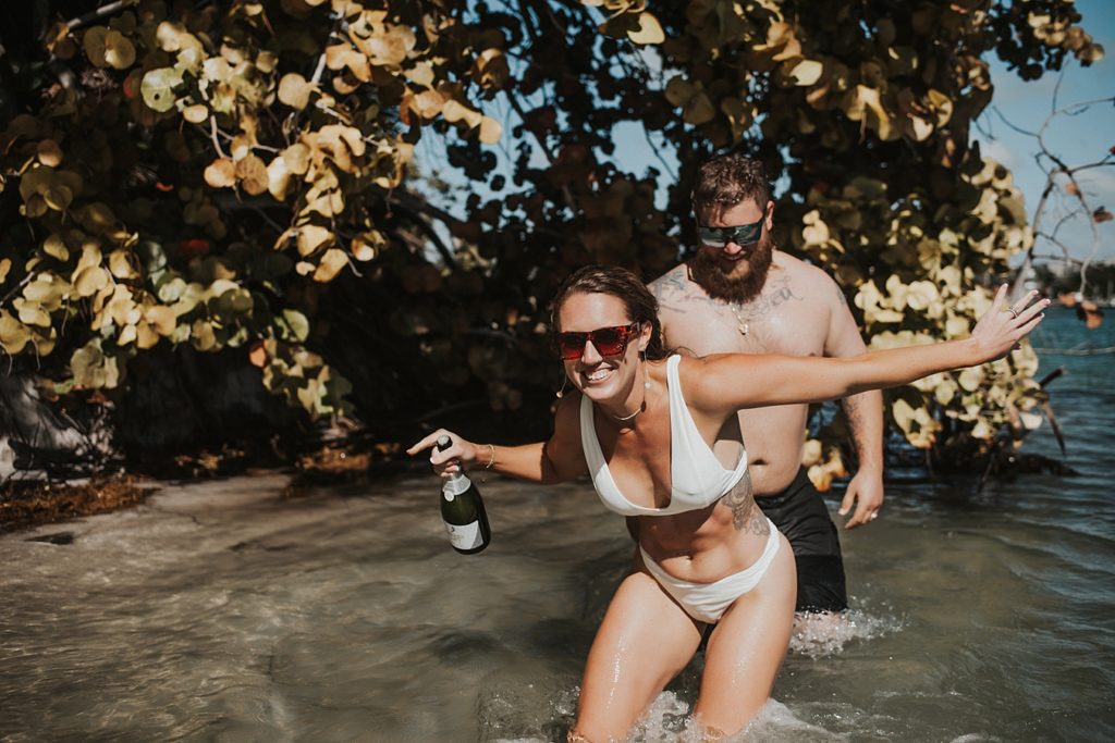 Bride popping champagne in water in front of mangroves