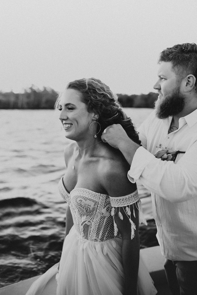 Bride smiling while groom puts on her necklace