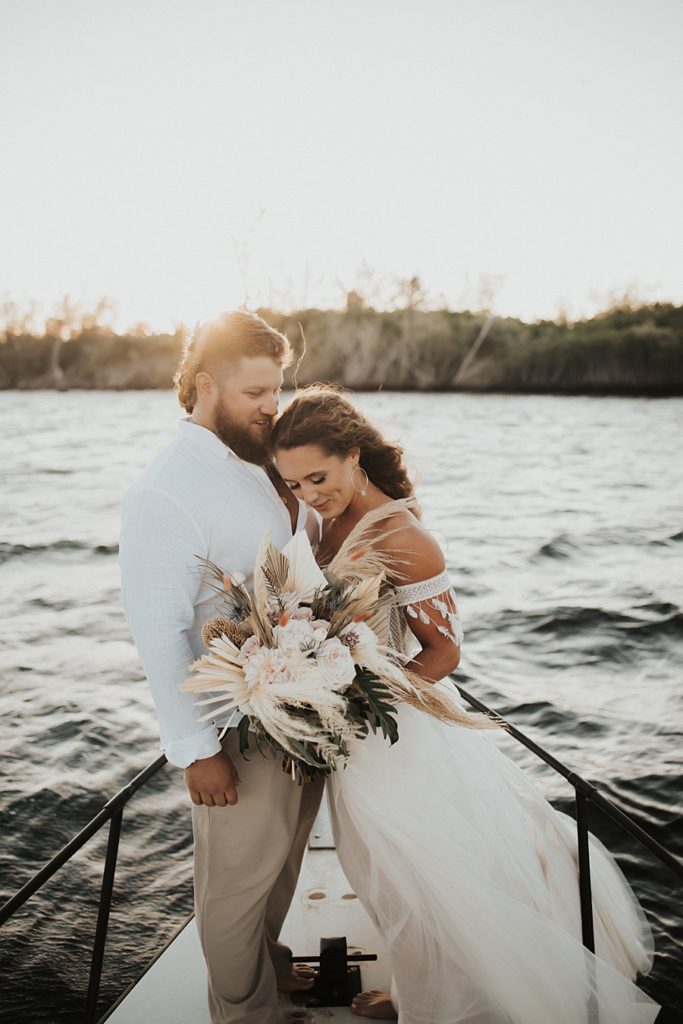 Bride and groom with dried floral bouquet on front of boat