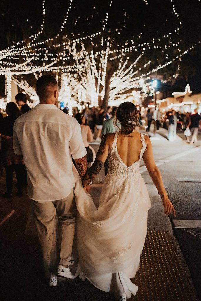Bride and groom walking night of lights while groom holds brides dress