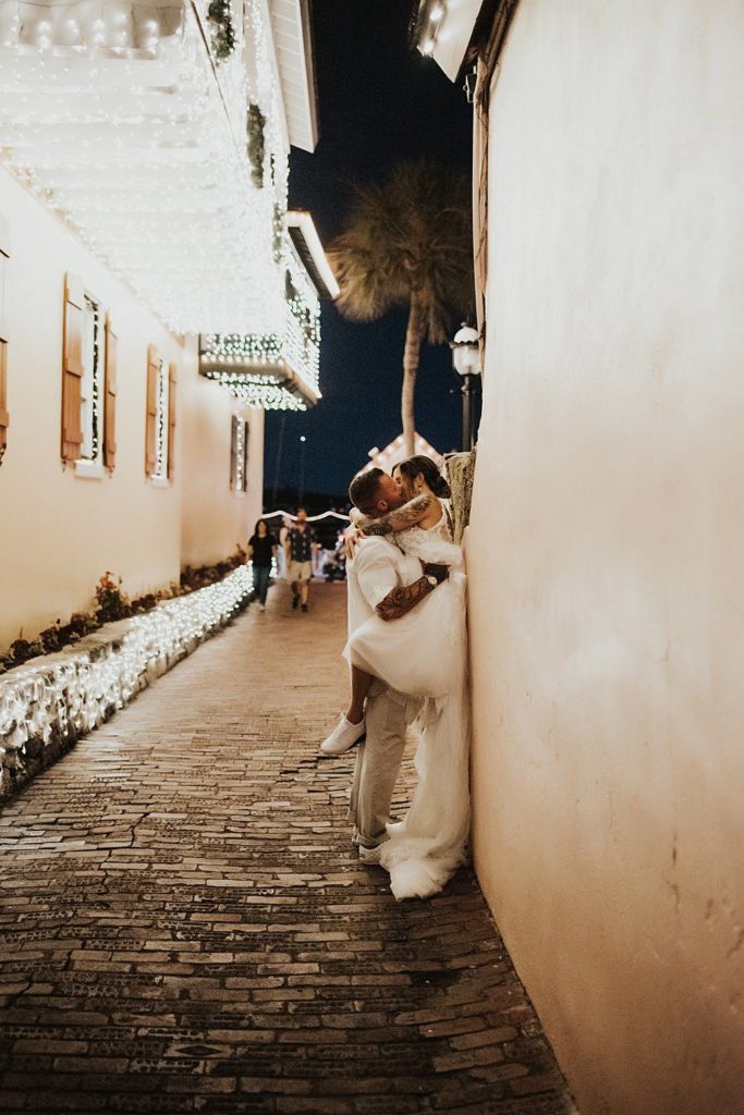 Groom picking up bride and pushing her against a wall in an alleyway