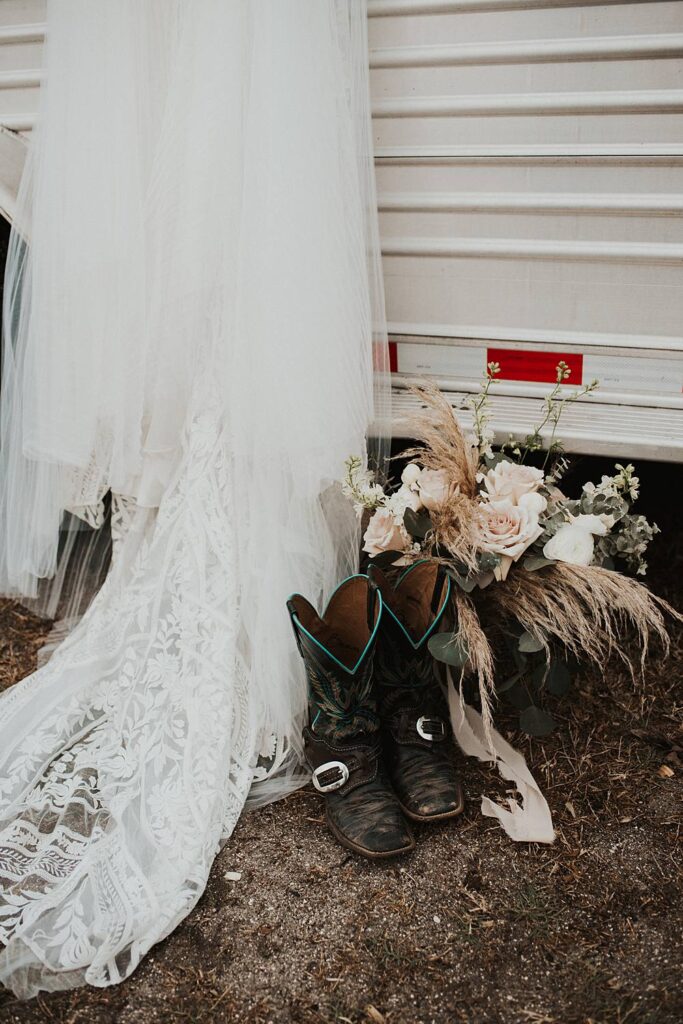 Brides wedding gown hung up with boots and flowers on the ground