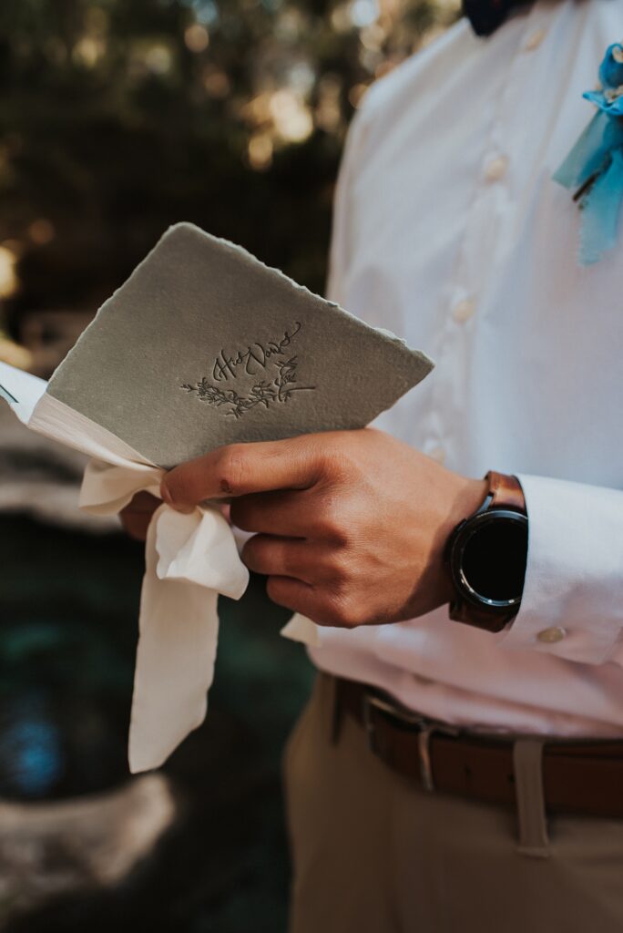 Paper and ribbon vow book in grooms hands