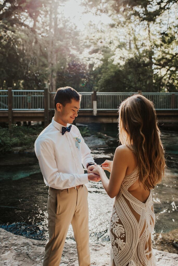 Bride and groom exchanging rings on rock surrounded by crystal clear blue water in Kelly Park Rock Spring 