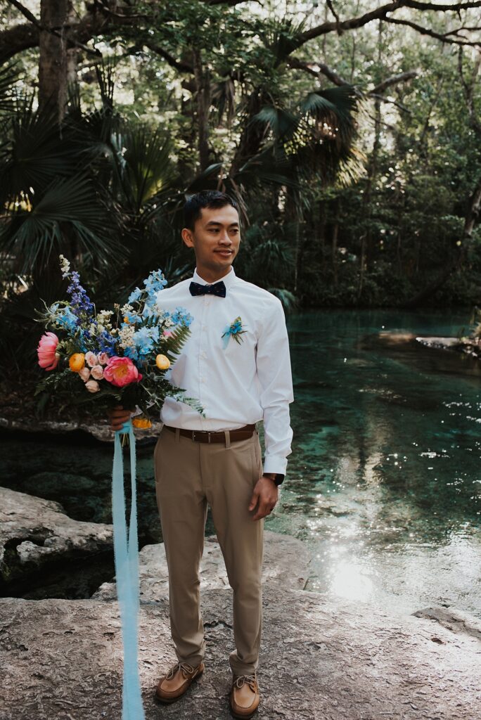 Groom with spring floral bouquet at Kelly Park Rock Springs in Apopka Florida during her elopement