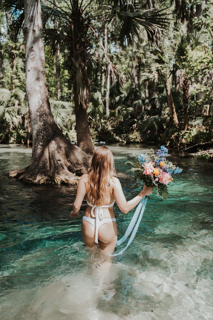 Bride in bikini getting into water at King's Landing with her spring-inspired bouquet 